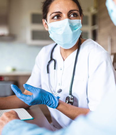 A doctor wearing a surgical mask and stethoscope talks to a patient out of shot