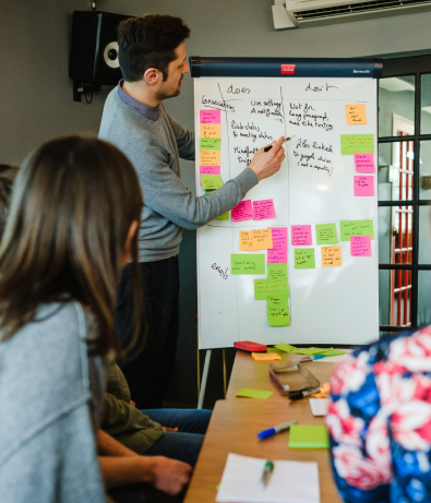 Graphite team member points at flip-chart with post-it notes stuck to it whilst someone else observes