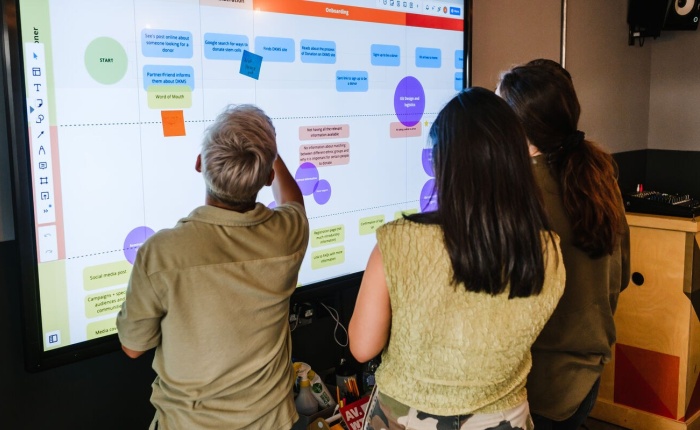 3 people looking at a large digital whiteboard which appears to be a design plan